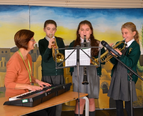 Three students playing trumpet and clarinet while their teacher plays piano