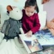 A young girl with a cuddly toy reading a book